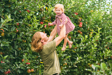 Happy young father playing with adorable baby girl outside, family lifestyle, dad holding kid high in the air, apple orchard