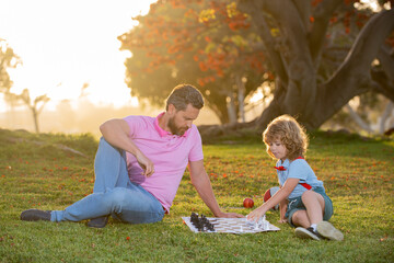 Father play chess with son. Thinking child while playing chess. Family outside game.