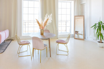 delicate and cozy light interior of the living room with modern stylish furniture of pastel pink color and white walls with stucco moldings in daylight