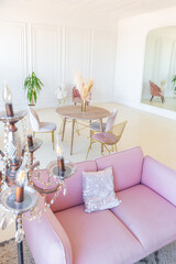 delicate and cozy light interior of the living room with modern stylish furniture of pastel pink color and white walls with stucco moldings in daylight