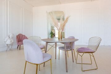 delicate and cozy light interior of the living room with modern stylish furniture of pastel pink color and white walls with stucco moldings in daylight