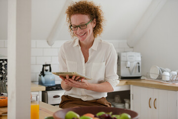 Portrait of woman sitting looking at digital tablet in kitchen,smiling