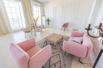 delicate and cozy light interior of the living room with modern stylish furniture of pastel pink color and white walls with stucco moldings in daylight