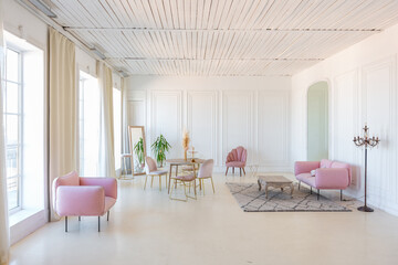 Fototapeta premium delicate and cozy light interior of the living room with modern stylish furniture of pastel pink color and white walls with stucco moldings in daylight
