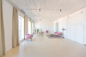 delicate and cozy light interior of the living room with modern stylish furniture of pastel pink color and white walls with stucco moldings in daylight