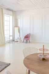delicate and cozy light interior of the living room with modern stylish furniture of pastel pink color and white walls with stucco moldings in daylight