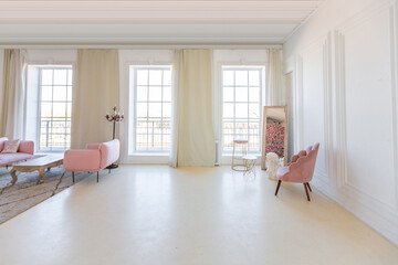 delicate and cozy light interior of the living room with modern stylish furniture of pastel pink color and white walls with stucco moldings in daylight