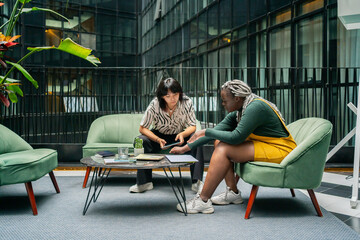 Two Women Sitting On A Couch In A Coworking Workplace. 