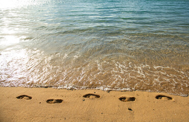Footprints at golden sand, footsteps. Tropical beach with sea sand on summer vacation.