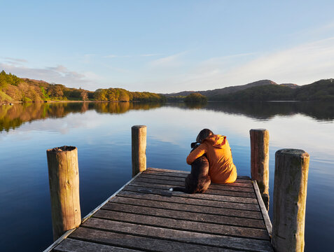 Female and her dog on a jetty at sunset. Coniston Water, Cumbria