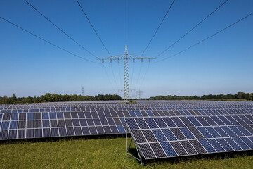 Renewable energy, electricity pylons in the middle of a large field of solar panels on a sunny day and blue sky