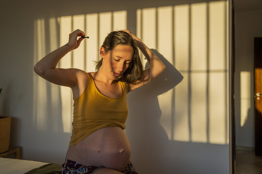 Gravid woman combing her short hair at bedroom