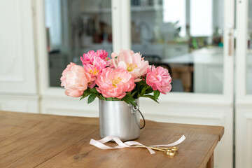 Closeup of a bouquet of pink peonies in a metal vase on the table with scissors and a ribbon on it © Elena Kloppenburg/Wirestock