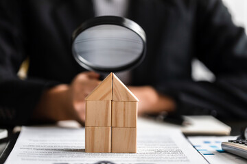Close up of businesswomen holding magnifying glass finding a wooden shape of a house, realtor,...