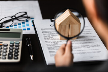 Close up of businesswomen holding magnifying glass finding a wooden shape of a house, realtor, agent, insurance, developer, planning and investment real estate business concept,