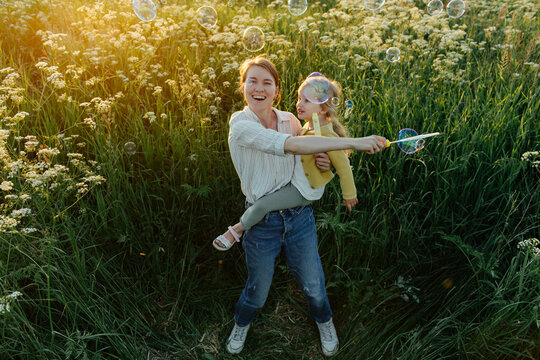 Joyful mother blowing soap bubbles with happy kid