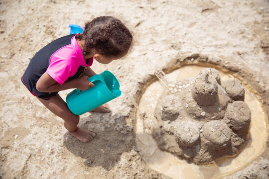 Toddler child pouring water into a sandcastle's trench