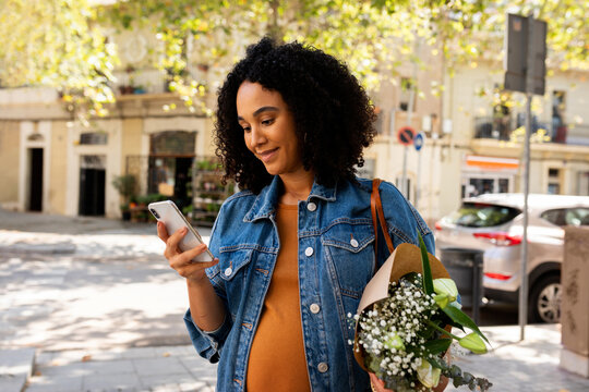 Pregnant woman with flowers using her phone outdoor