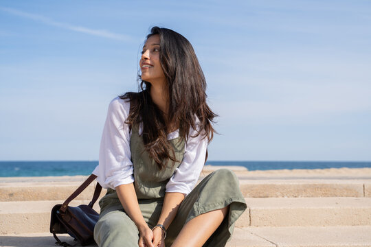 Smiley young woman  sitting on staris by the sea