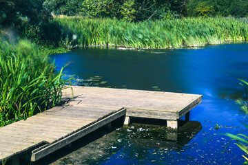 Calm still water with wooden jetty in the foreground - obrazy, fototapety, plakaty