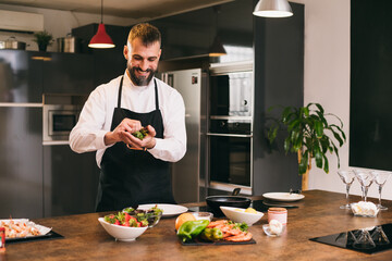 Positive chef preparing fresh herbs for dish 