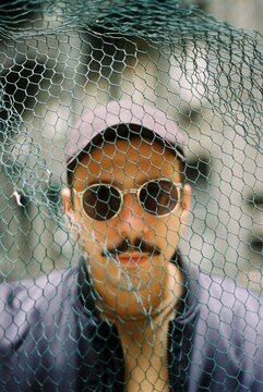 A man with sunglasses in front of a green wire.
