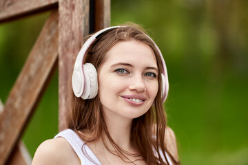 Wireless headphones on pleasant young woman in park.