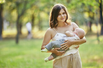 Breastfeeding in public park, young mother feeds her baby in nature.