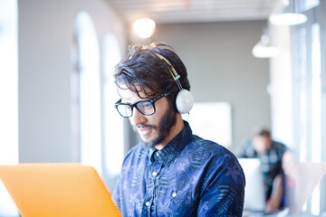 Casual businessman wearing headphones and using laptop in office
