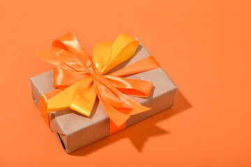 Gift box with an orange satin bow on an orange background with a place for text.