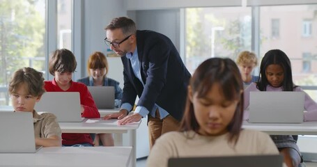 Diverse teenage students working on laptop in classroom and mature teacher help - Powered by Adobe