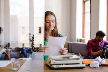 Obraz na płótnie Canvas Creative businesswoman reviewing paperwork at typewriter in office