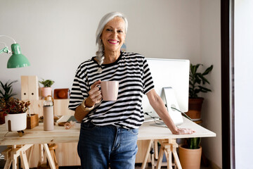 Hoary woman with a coffee cup smiling at modern studio