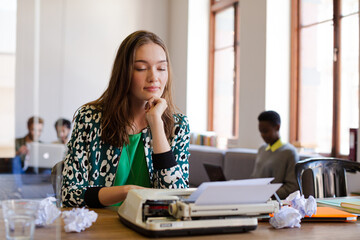 Creative businesswoman reviewing paperwork at typewriter in office