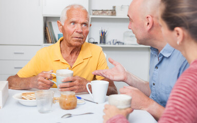Portrait of mature man with daughter and friend talking at table with cup of tea