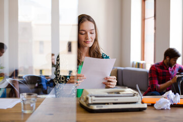 Creative businesswoman reviewing paperwork at typewriter in office