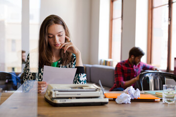 Creative businesswoman reviewing paperwork at typewriter in office