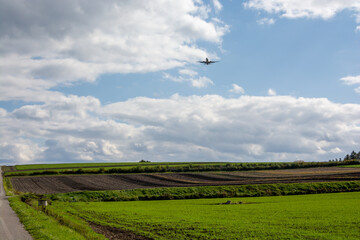 緑の畑作地帯を飛ぶジェット旅客機
