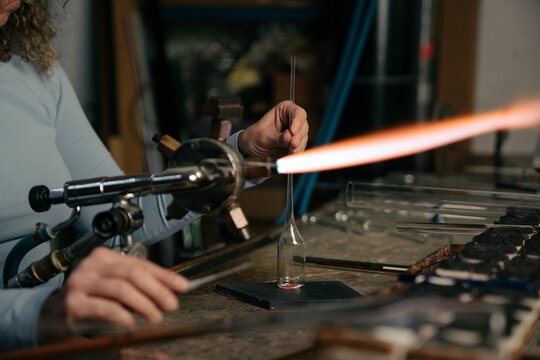 Close up of a lampworker working with torch flame and glass tube shaping