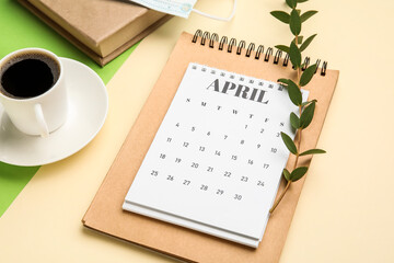 Calendar with cup of coffee and notebook on color background