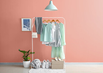 Rack with stylish clothes and shoes near color wall