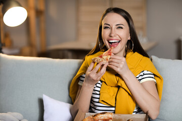 Beautiful young woman eating tasty pizza while watching TV at home in evening