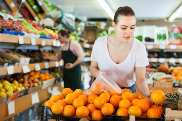 Glad woman customer choosing fresh oranges on the supermarket