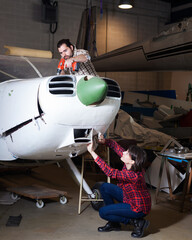 Female and male amateurs engaged in restoring old light plane in aircraft workshop