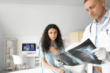Mature doctor showing x-ray image of lungs to patient in clinic - Powered by Adobe