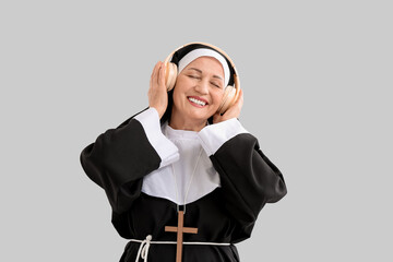 Mature nun with headphones listening to music on light background