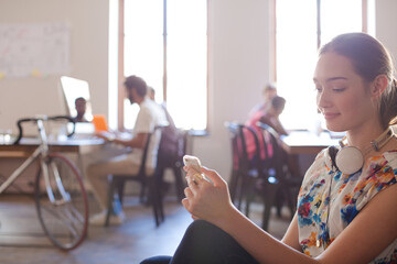 Obraz na płótnie Canvas Casual businesswoman headphones texting cell phone in sunny office