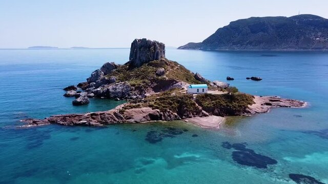 Cinematic drone shot of paradisiacal greek island with a small church on it.