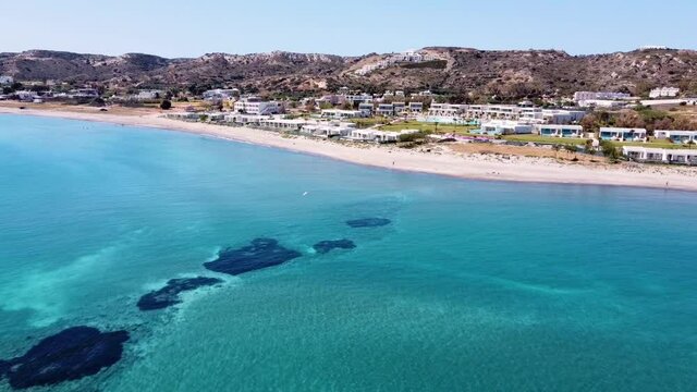 Cinematic drone shot of paradisiacal greek beach with a beautiful sea and some houses on the shore.