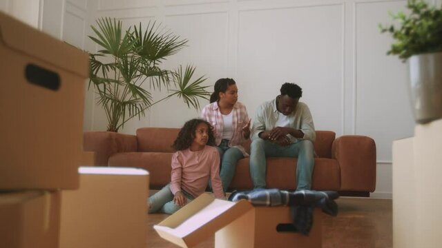 Young nervous african american parents quarreling in new home, sad little girl sitting on floor among cardboard boxes